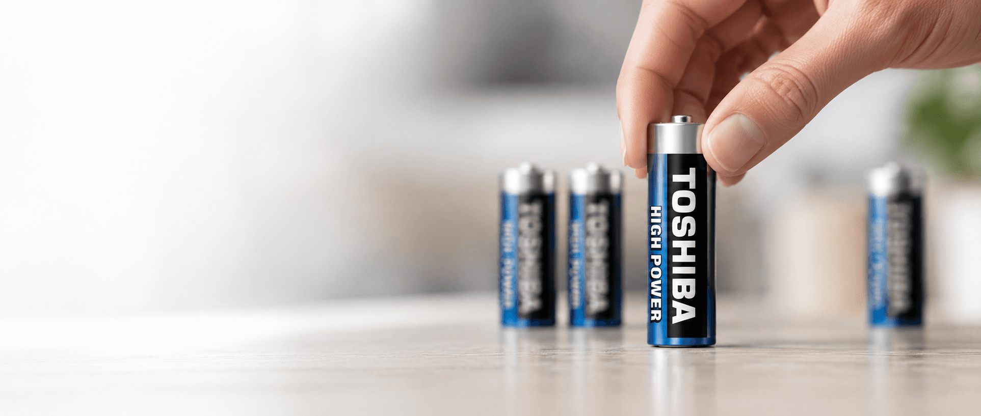 Hand placing a Toshiba High Power AA battery on a tabletop.